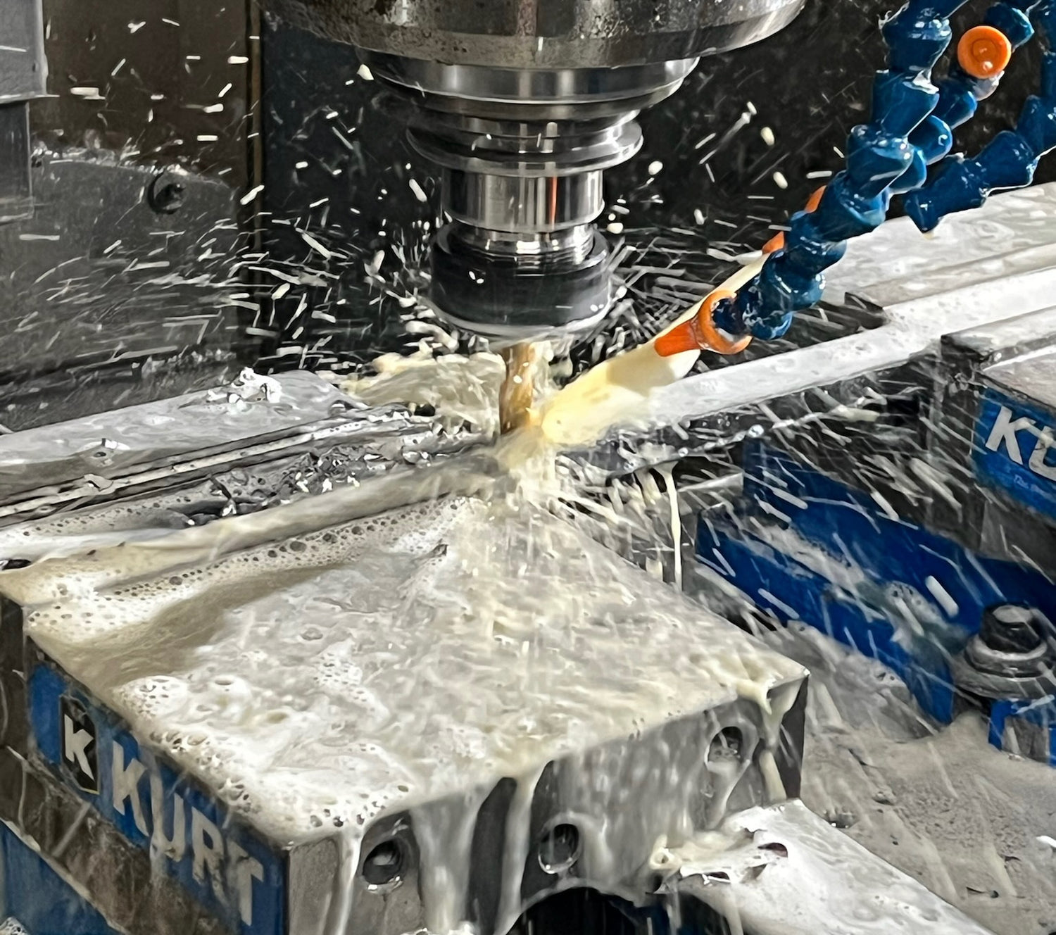 CNC machine in operation with coolant spraying over a metal component.